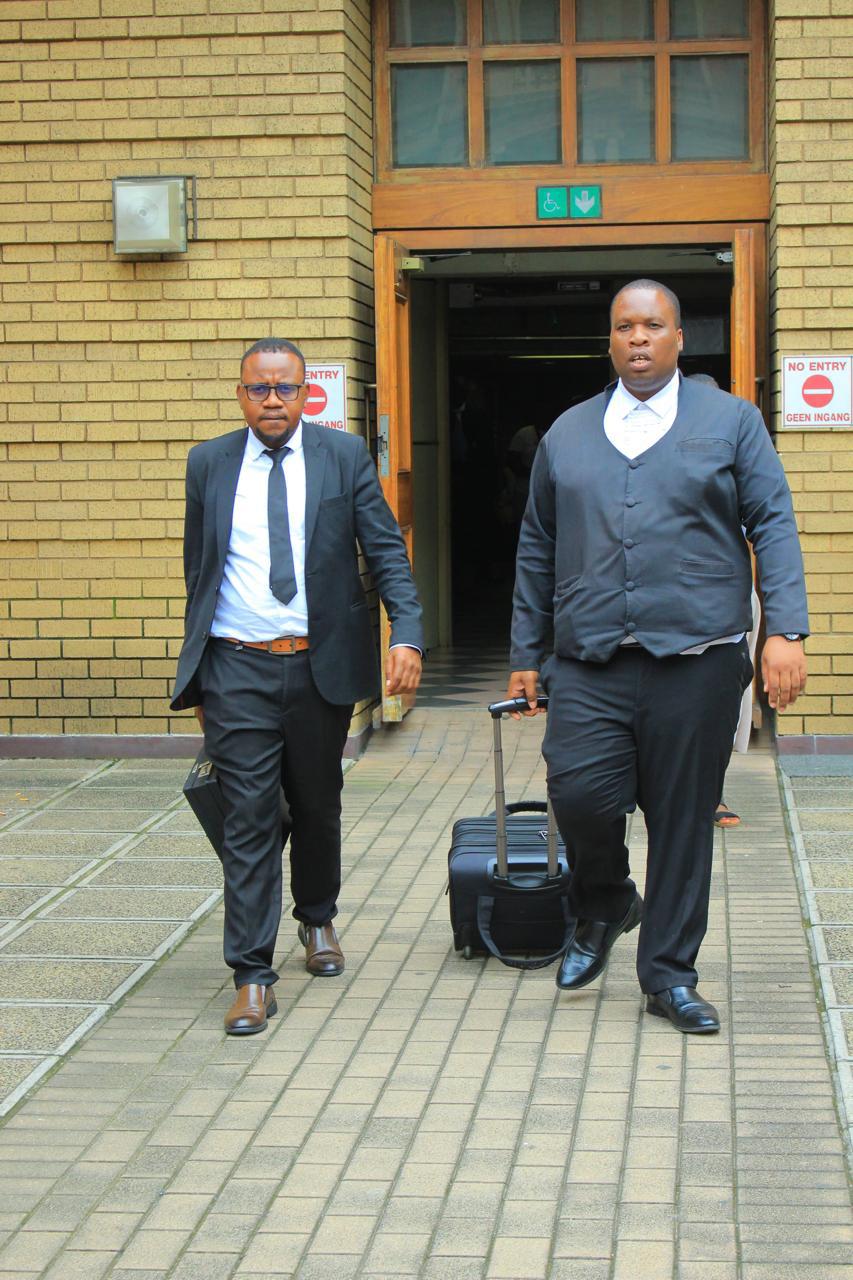 Two Hanyani attorneys leaving the Magistrates' Court entrance in Gauteng with case files and a wheeled trial bag