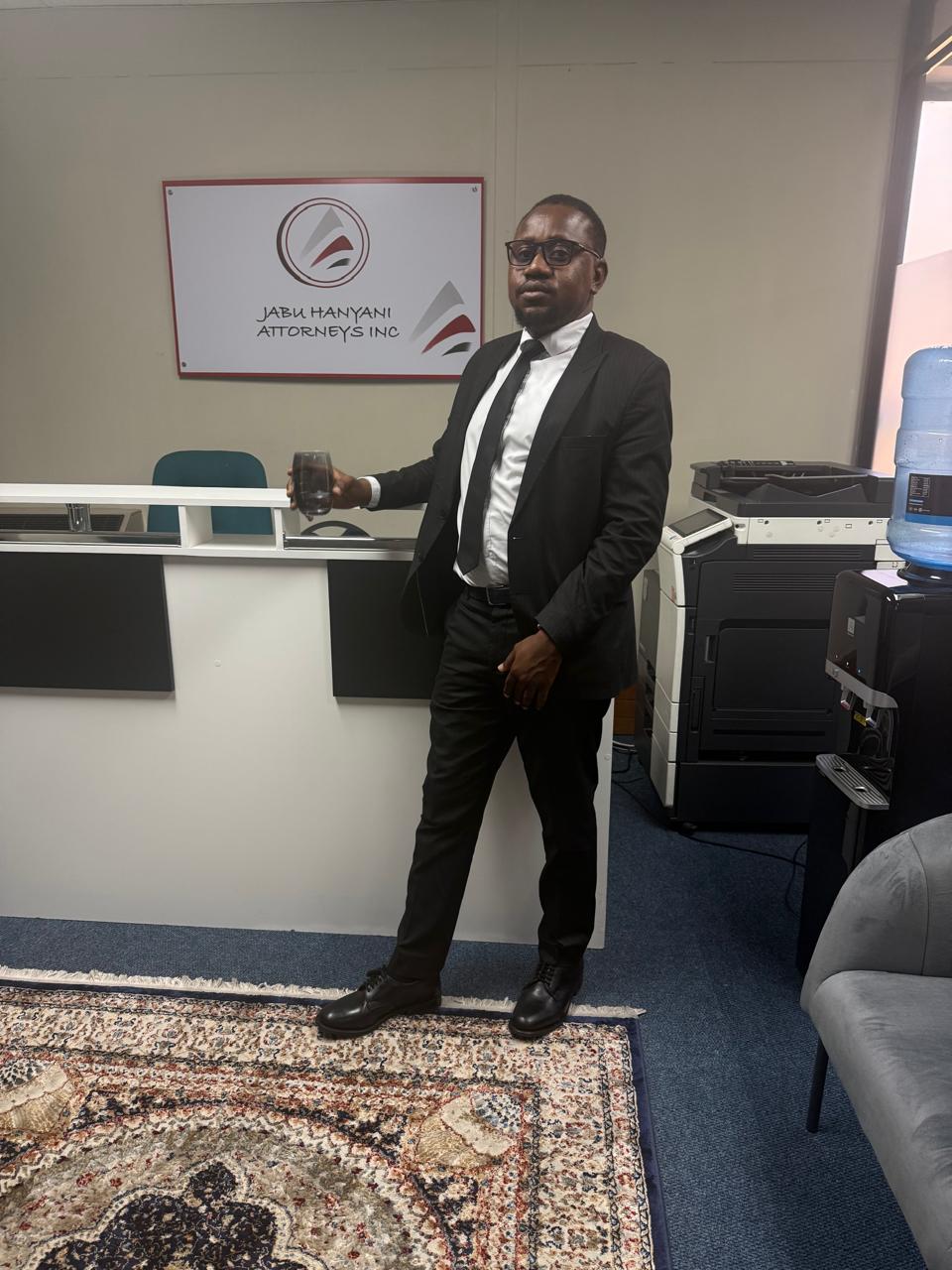 Jabu Hanyani standing beneath the Jabu Hanyani Attorneys Inc reception sign at the firm's Midrand chambers